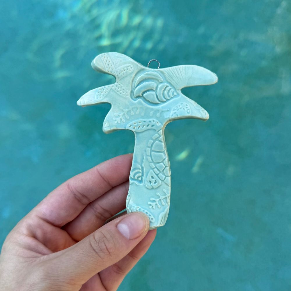Decorative palm tree ornament held against a teal water background. Sunshine Pot-Tree, Sunshine Coast, Qld